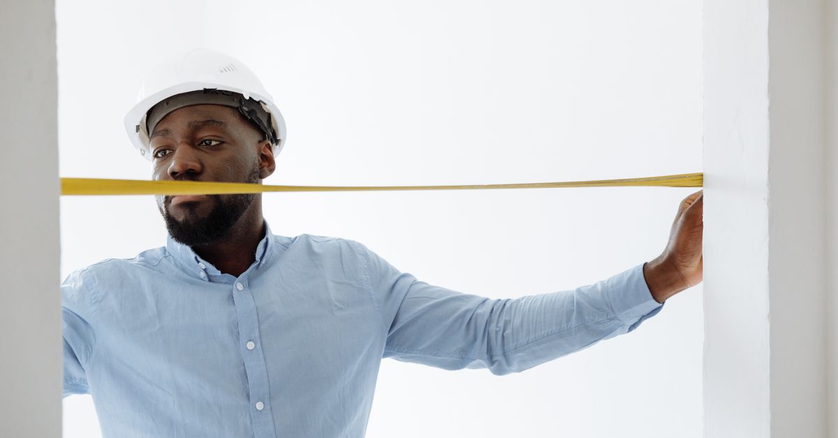 A contractor with a tape measure at a fence line