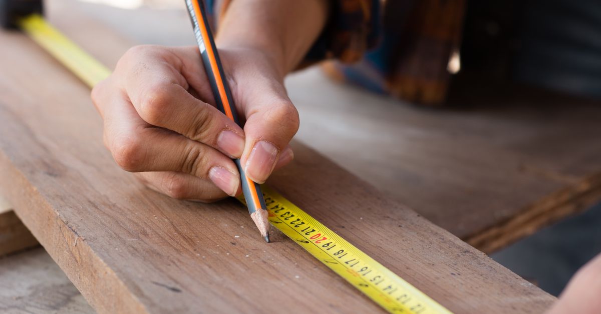 A contractor with a tape measure at a fence line