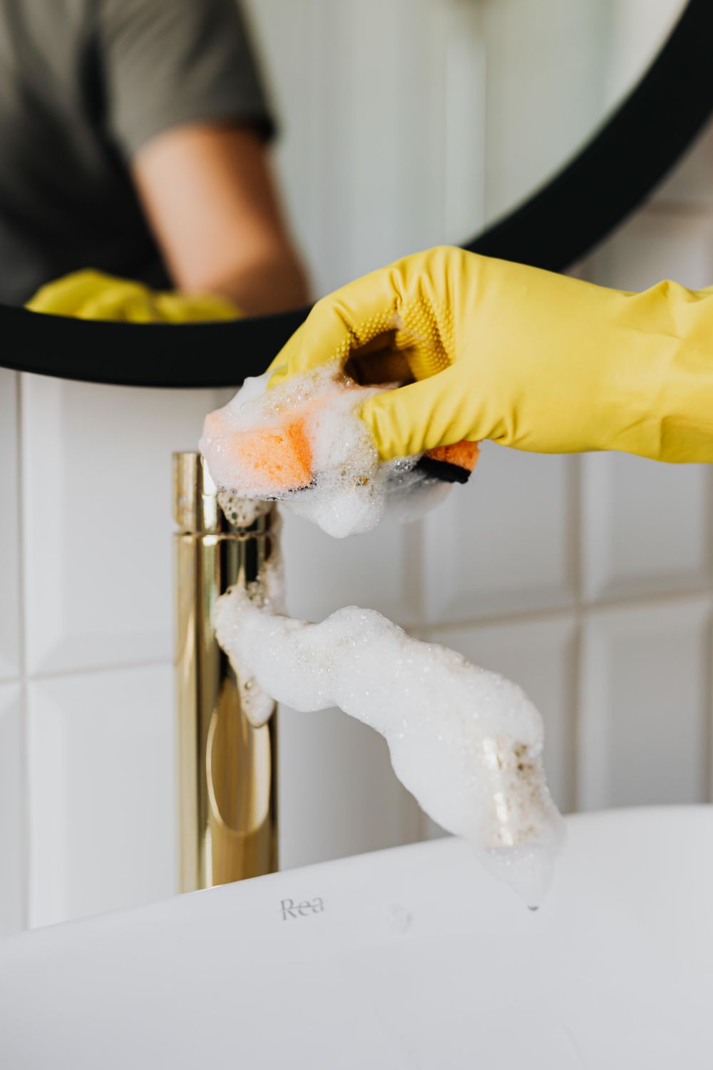 A gloved hand scrubbing a faucet during a move-out clean