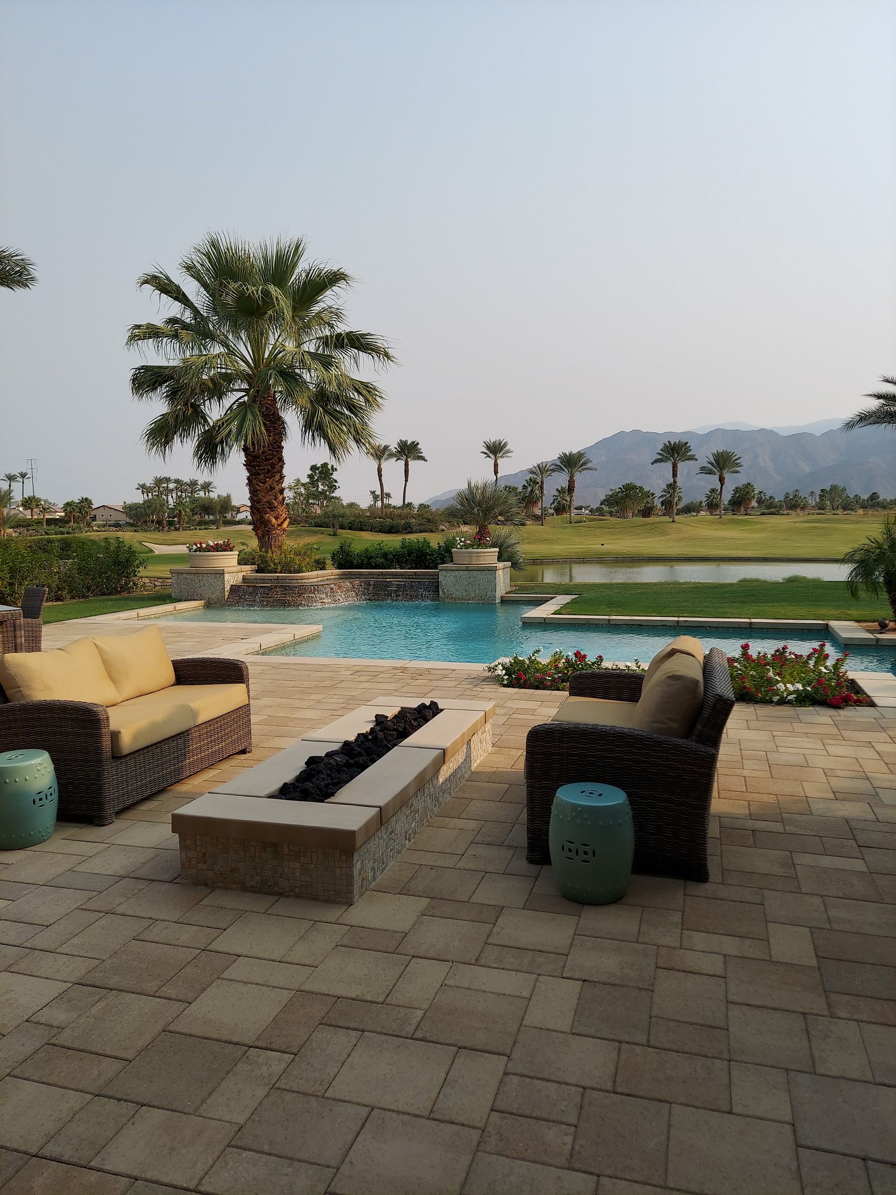 A desert backyard with a paver pool deck, palm trees, and mountain views