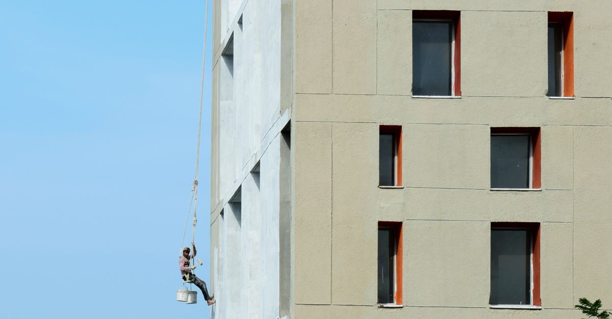 A painter rolling exterior paint on a stucco home